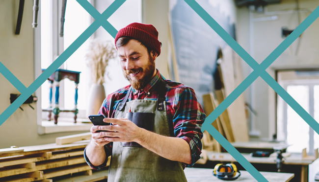 Happy local service business owner checking PPC advertising results on a smartphone in his workshop